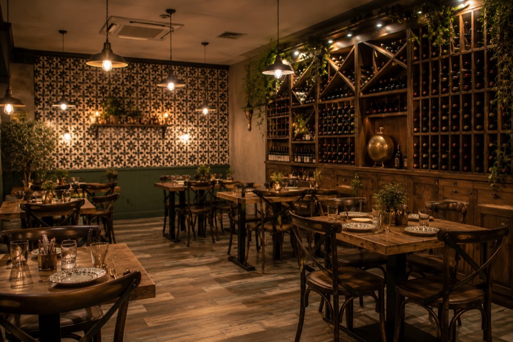 Дървени маси под топла светлина, с нашата плочка на стената / Wooden tables under warm light, our signature tile wall behind